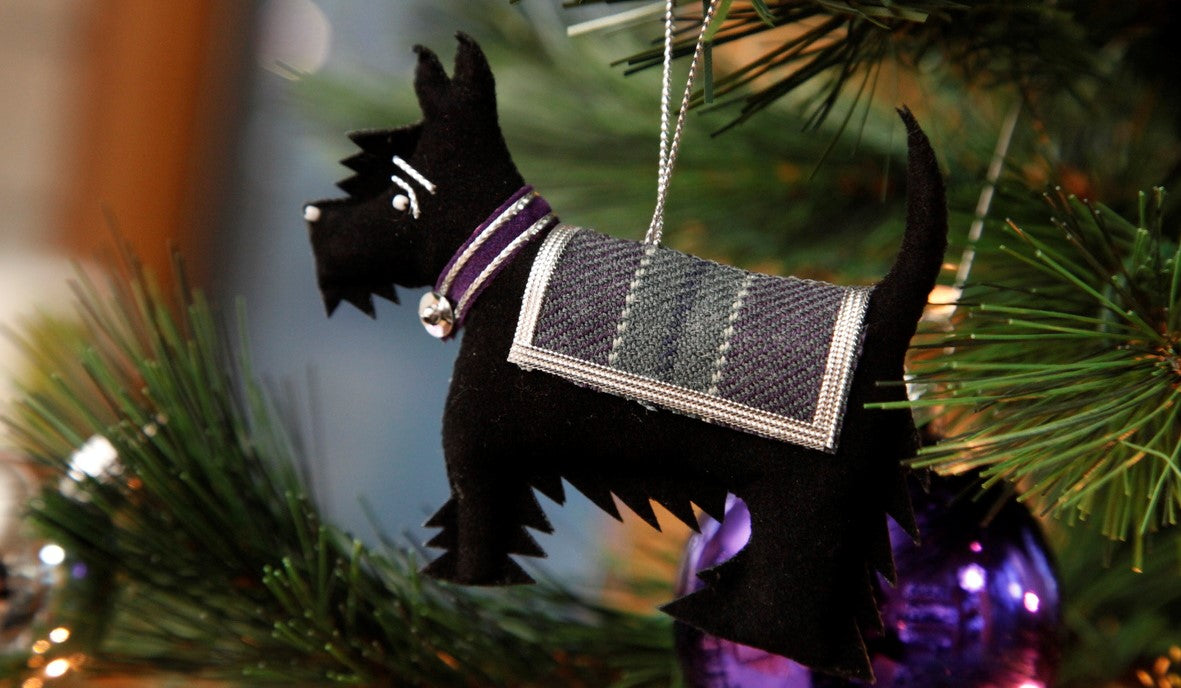 A close up photo of a christmas tree decoration shaped like a black Scottie dog decorated with the parliament tartan.