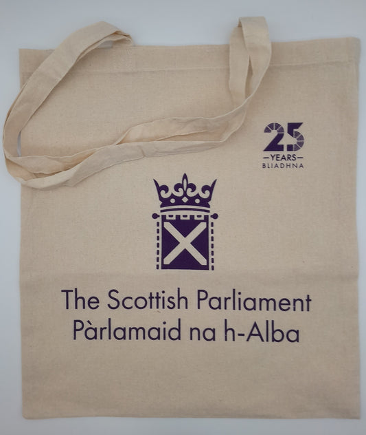 A light coloured cotton tote bag with the symbol of the Scottish Parliament and the 25th anniversary logo in purple. 