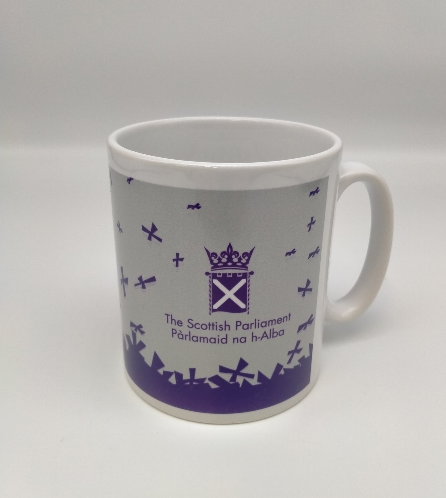 White mug printed with with purple Parliament symbol and saltires on grey background.