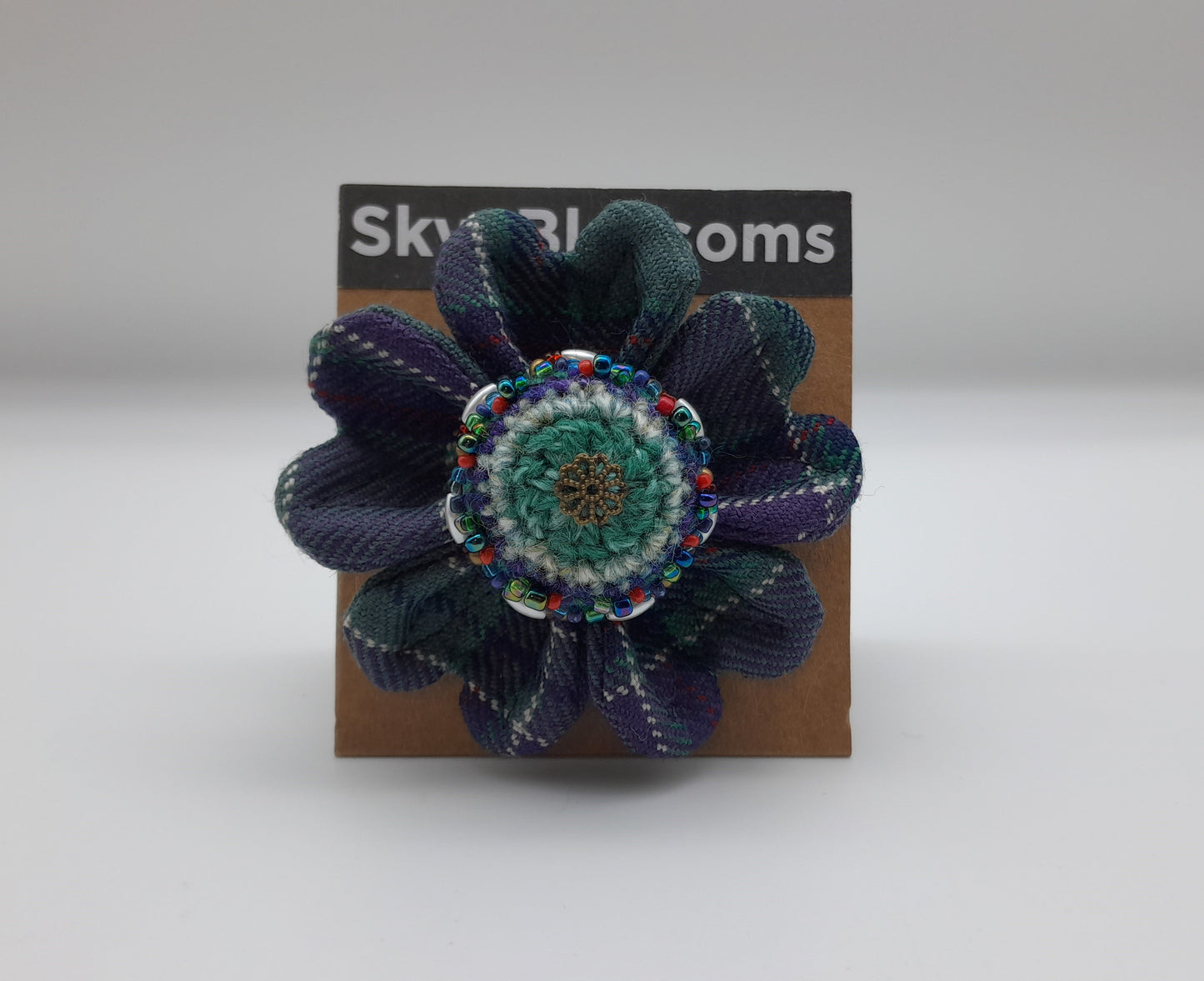 Green and purple tartan flower shaped brooch with decorative beads.