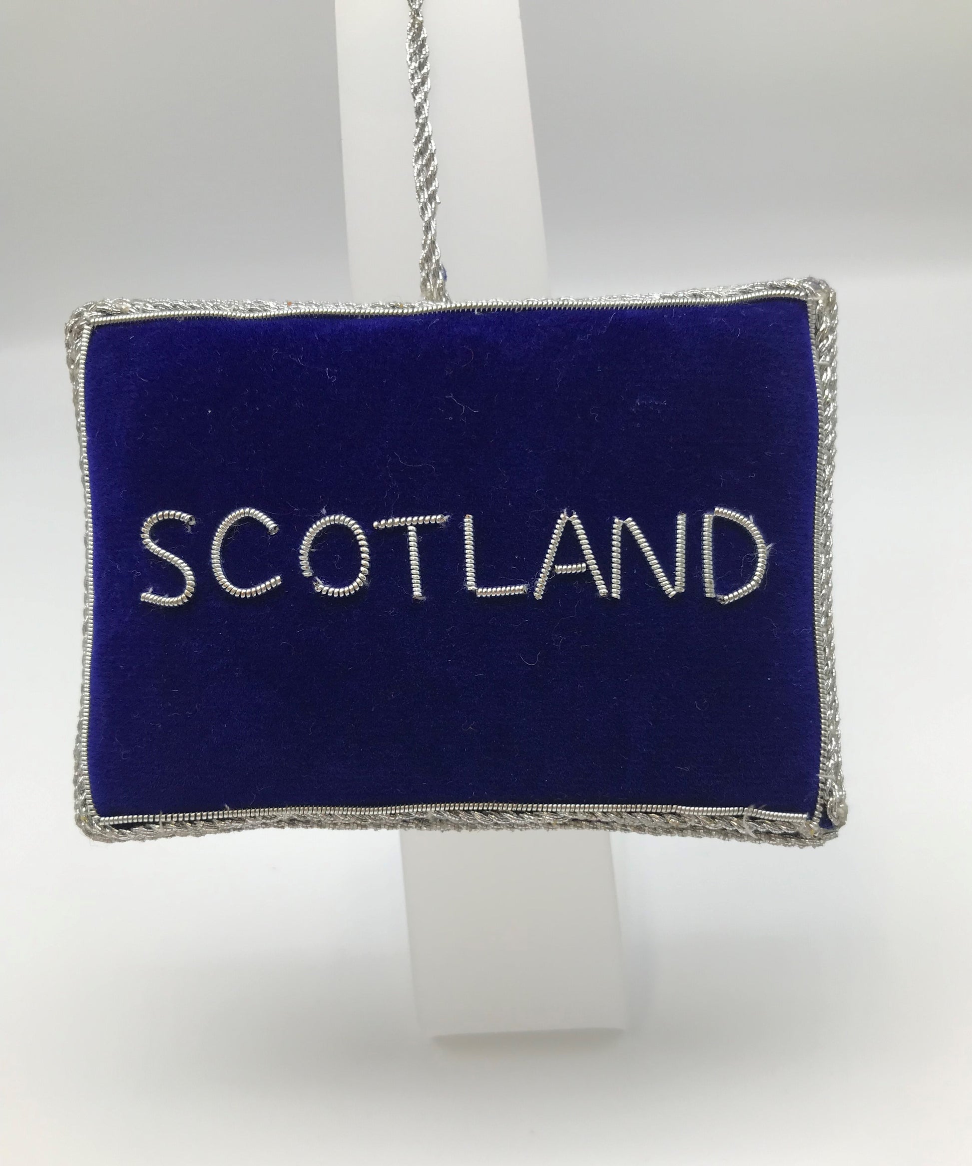 Rectangular decoration in dark blue fabric with Scotland embroidered in silver and silver stitching. 