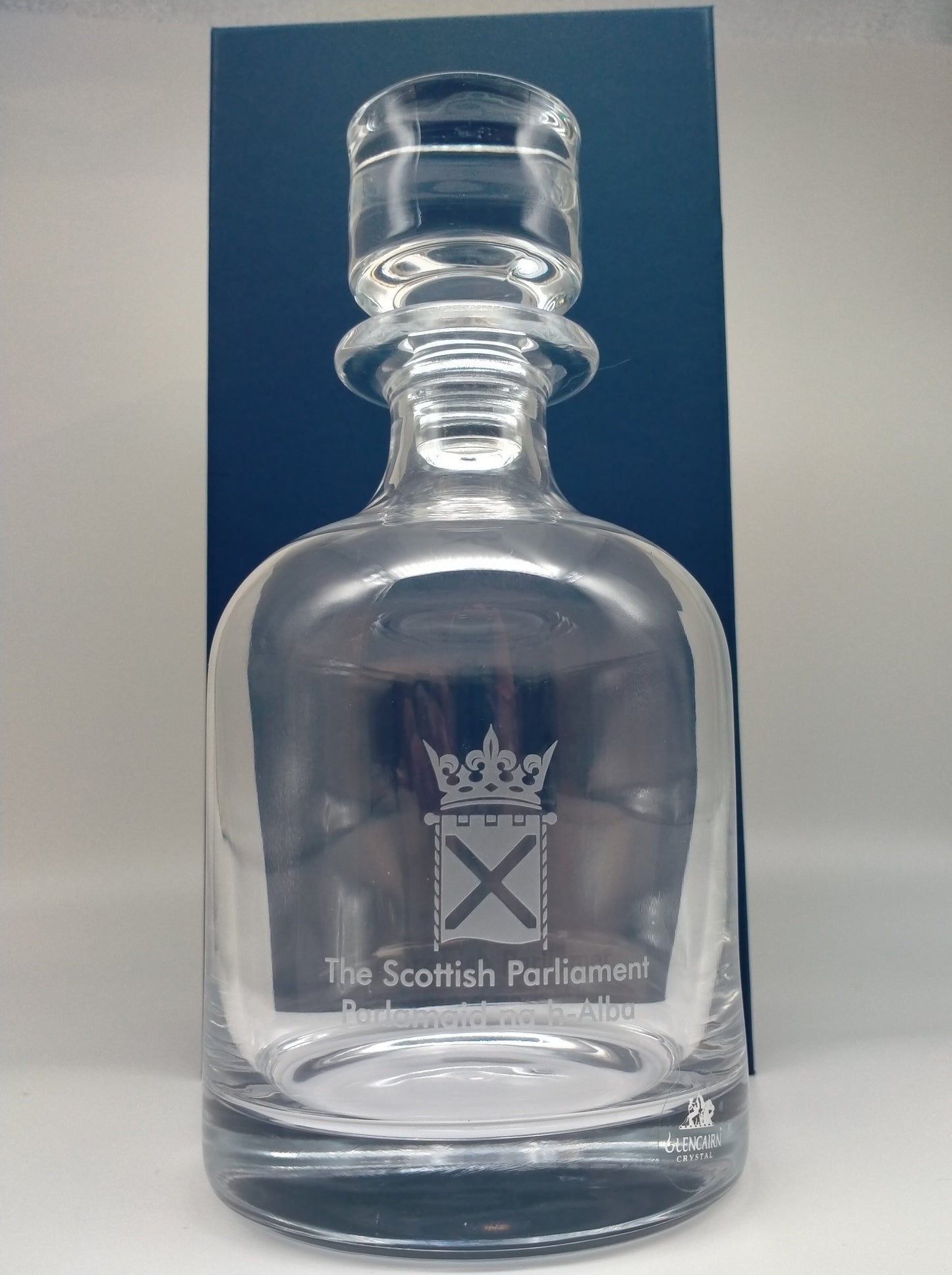 A crystal decanter engraved with the symbol of the Scottish Parliament in front of blue box.