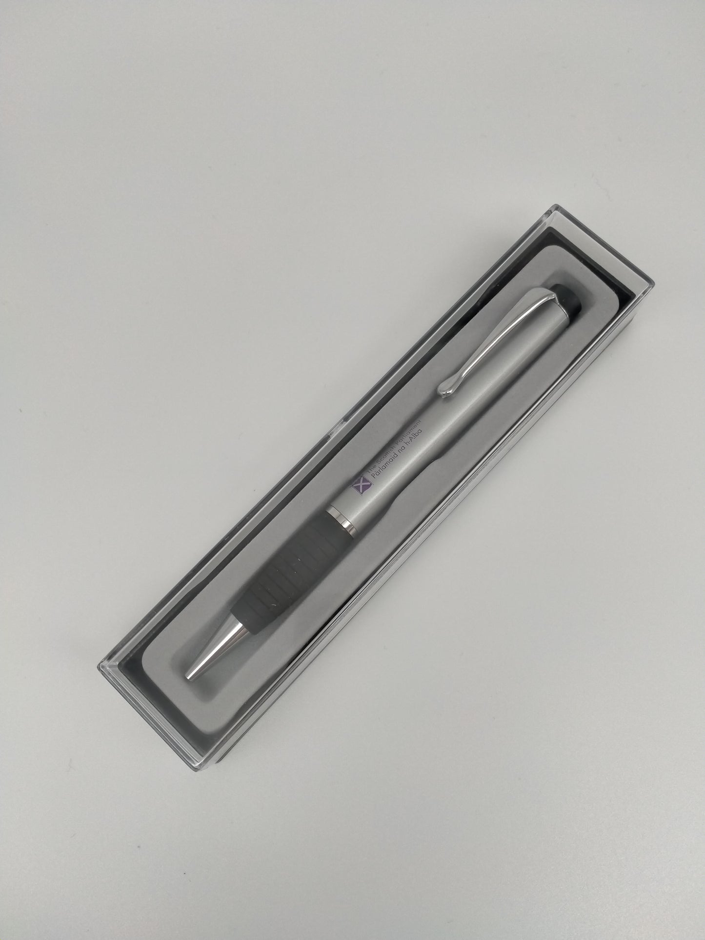 The pen inside its rectangular box with transparent lid.