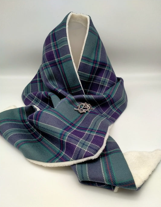 A woollen scarf in the official Scottish Parliament tartan, showing the white fleece lining. Draped, fastened and secured with a brooch.