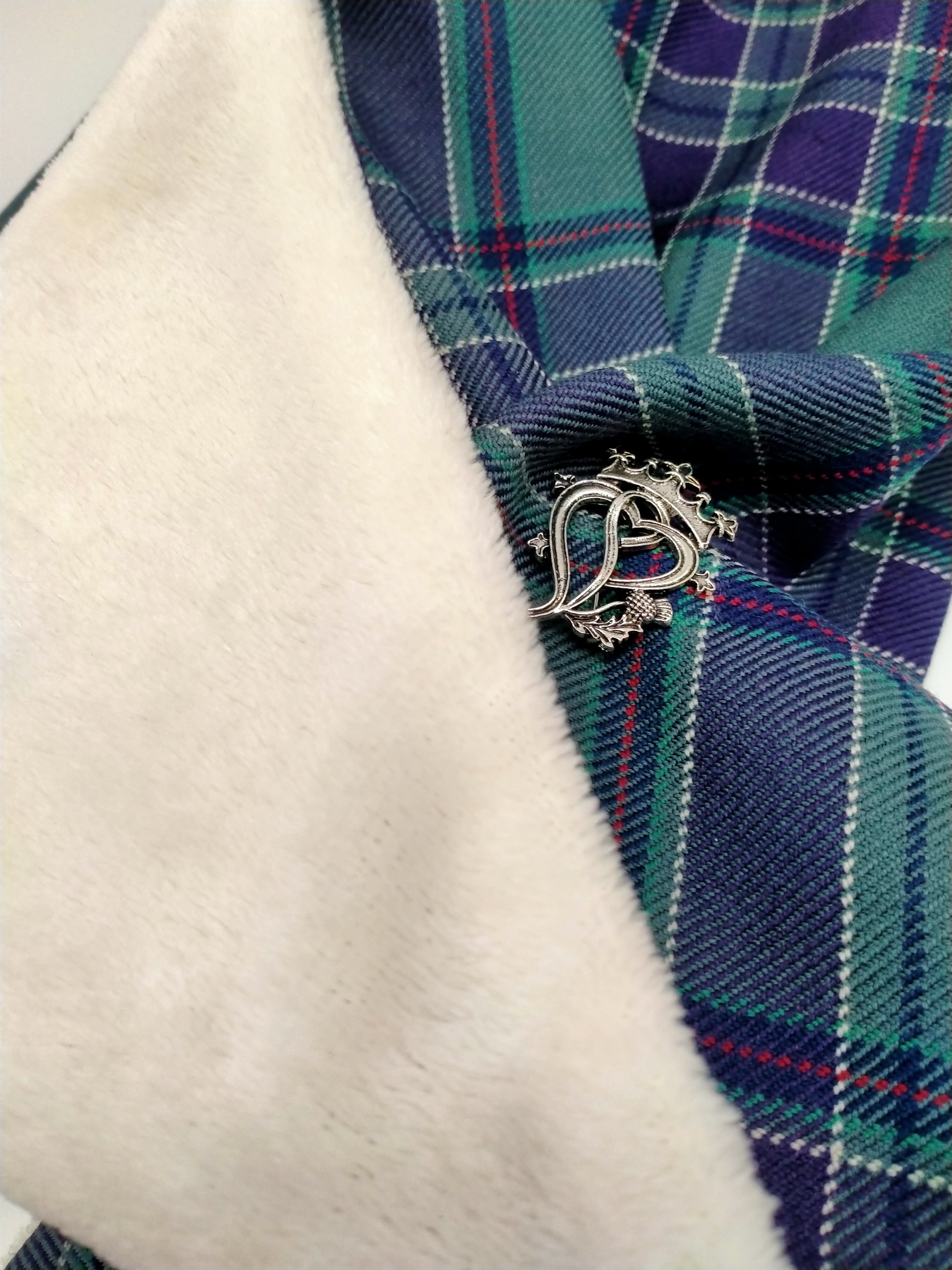 Close up photo of the woollen tartan fabric, the fleece lining and the brooch.