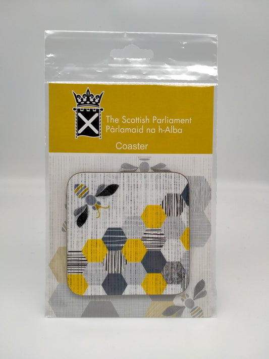 A square coaster printed with an image of a bee and and honeycomb in light and dark grey and yellow. In plastic bag.