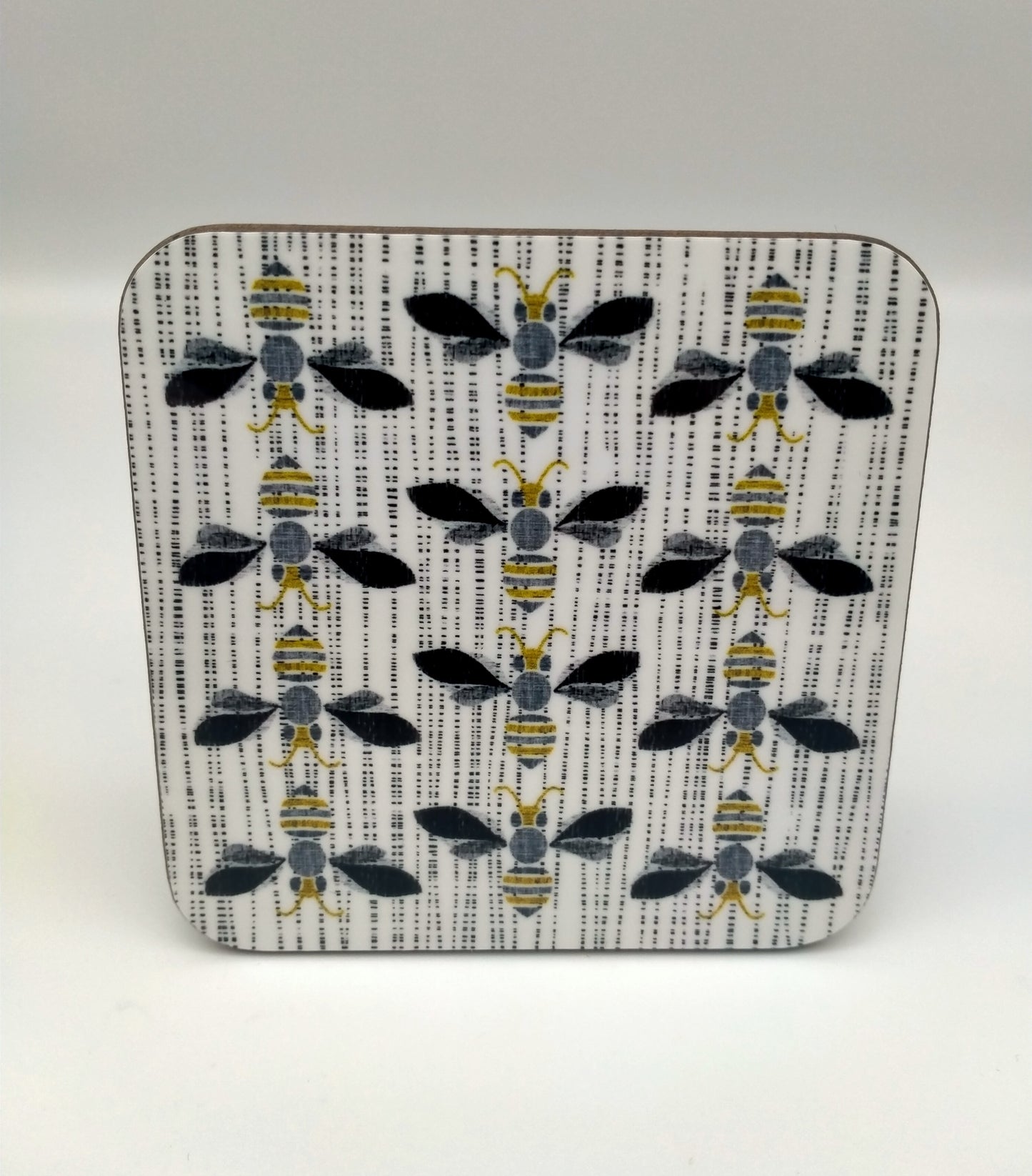 Square coaster with design of bees in three rows. Grey, black, gold tones.