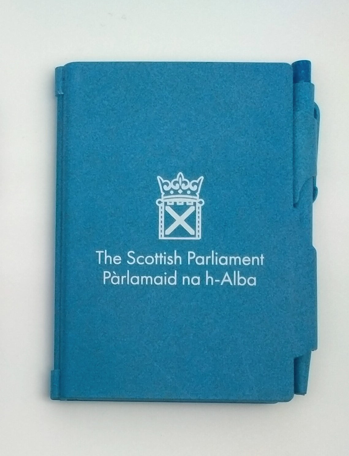 A blue notebook with the symbol of the Scottish Parlaiment in white and a matching pen slid into a holder on the side.
