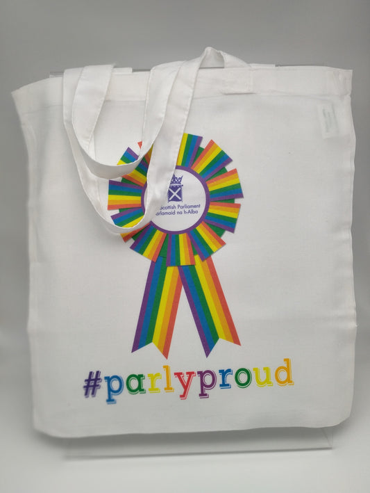 A white cotton bag printed with a rainbow rosette with the purple symbol of the Scottish Parliament in the middle, and with the words '#parlyproud' in rainbow colours.