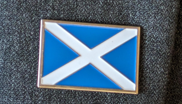 Rectangular badge. Blue background with a white cross. Sitting on a grey fabric background