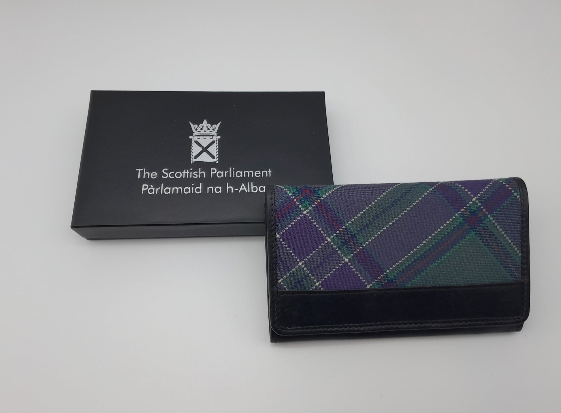 The purse next to its black box. The lid is decorated with the symbol of the Scottish Parliament printed in silver.