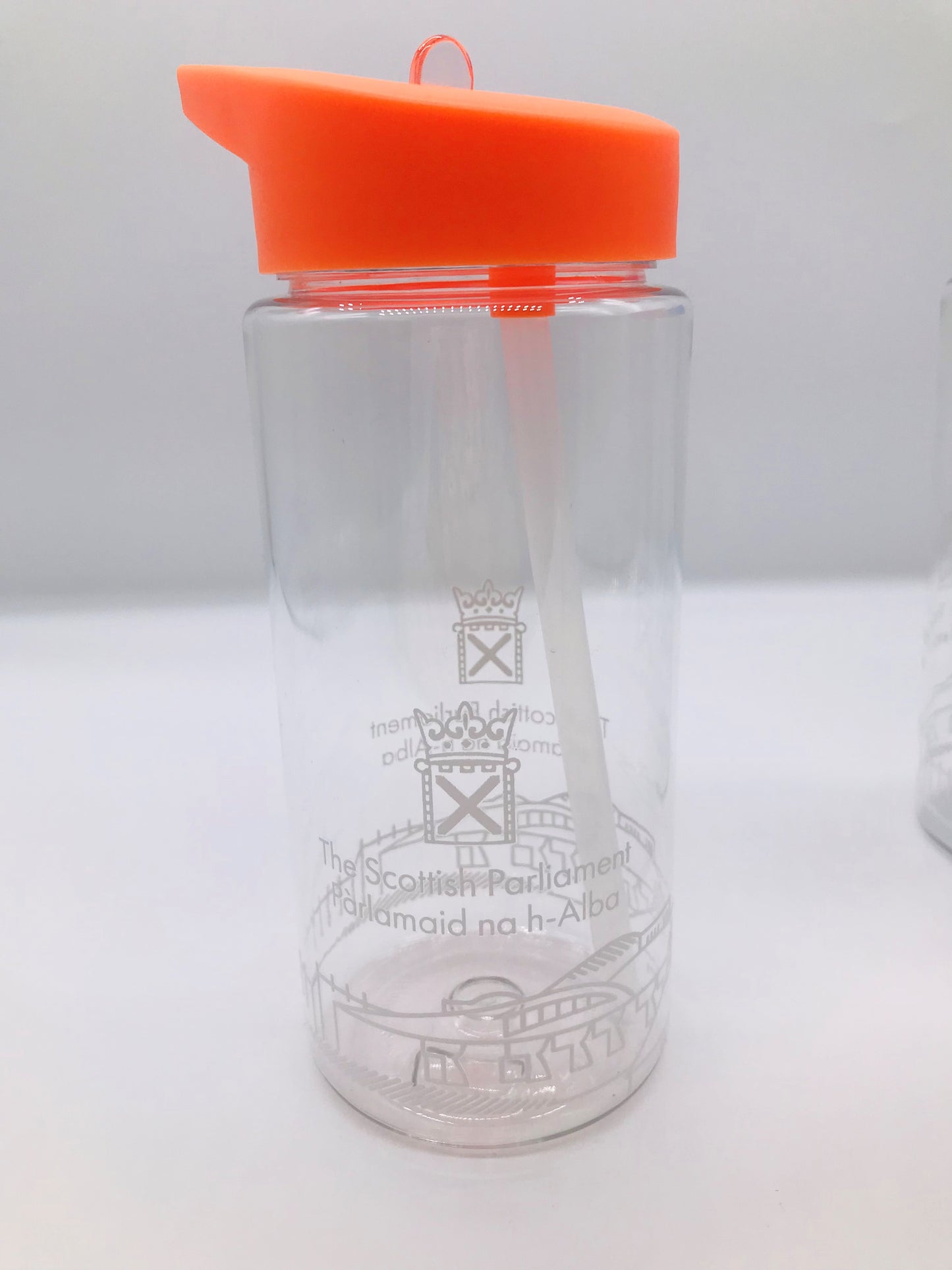 A clear plastic bottle with internal straw. it has the Scottish Parliament logo and outline of the parliament building painted around the circumference of the bottle. Its lid is orange