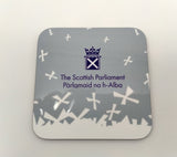 A square coaster with the symbol of the Scottish Parlaiment and white saltires on grey background.