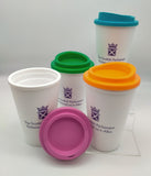 Four white cups with lids in different colours. Decorated with the symbol of the Scottish Parliament in purple. One cup with a lid taken off.