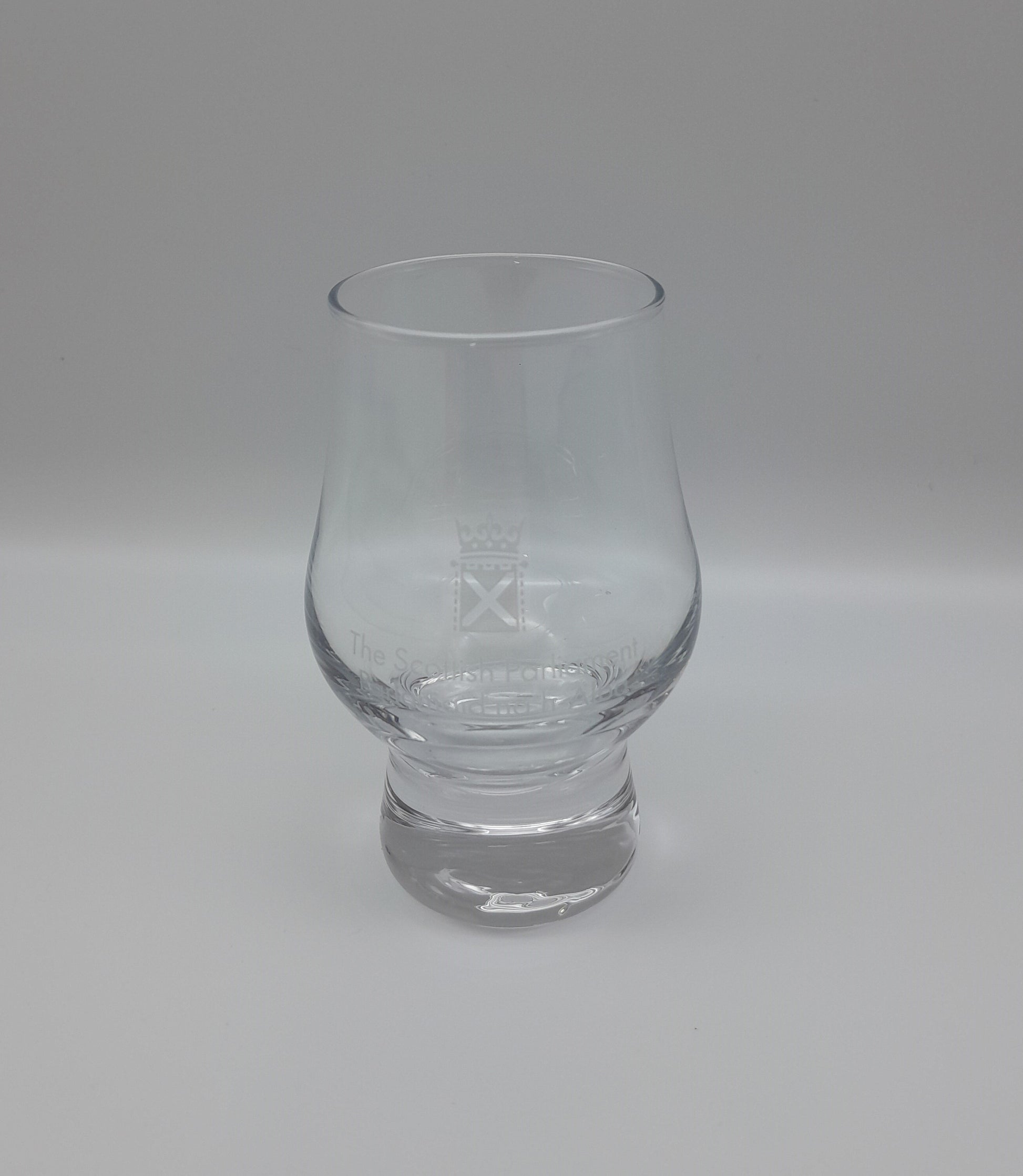 A small tulip shaped whisky glass decorated with the symbol of the Scottish Parliament.