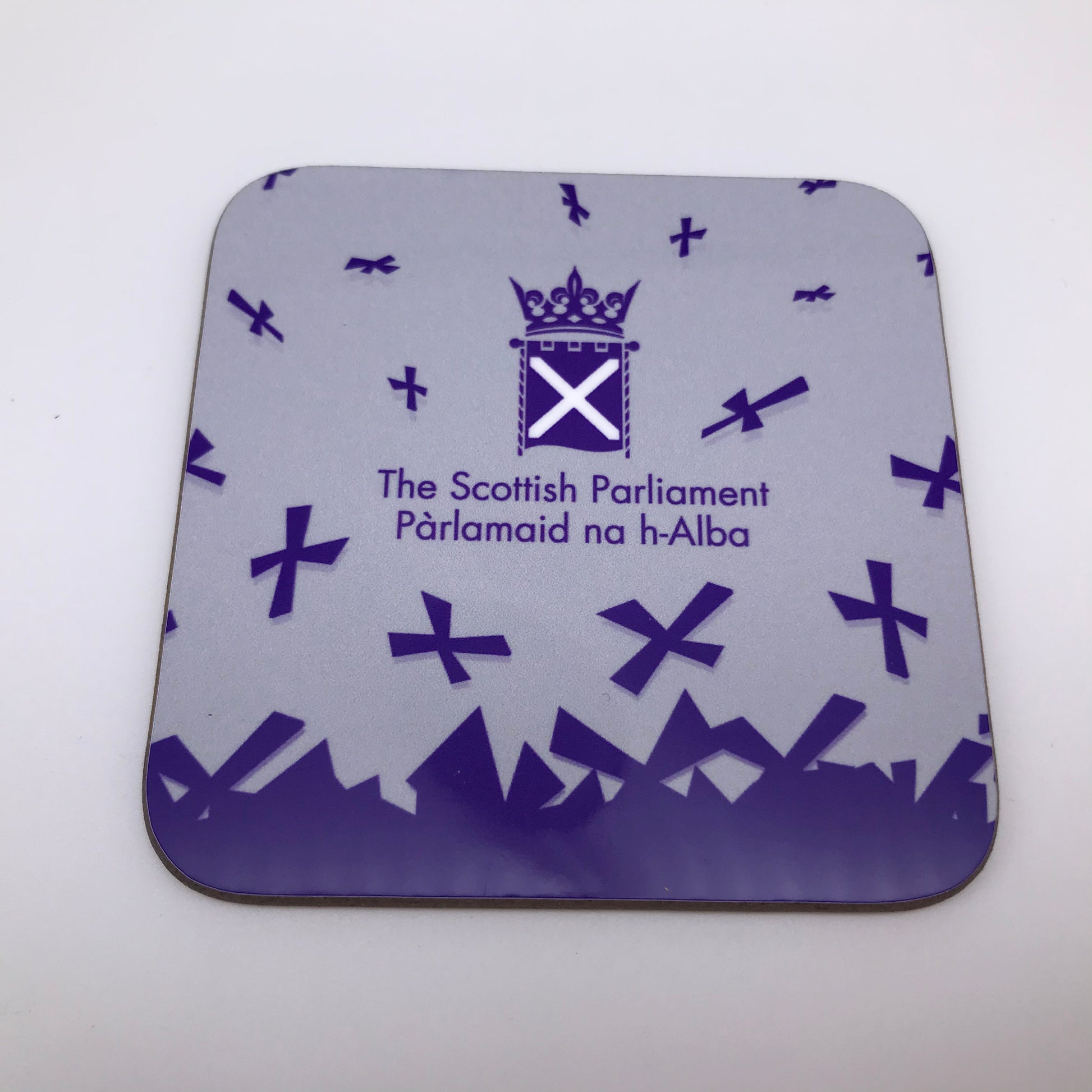 A square coaster with the symbol of the Scottish Parliament and purple saltires on grey background.