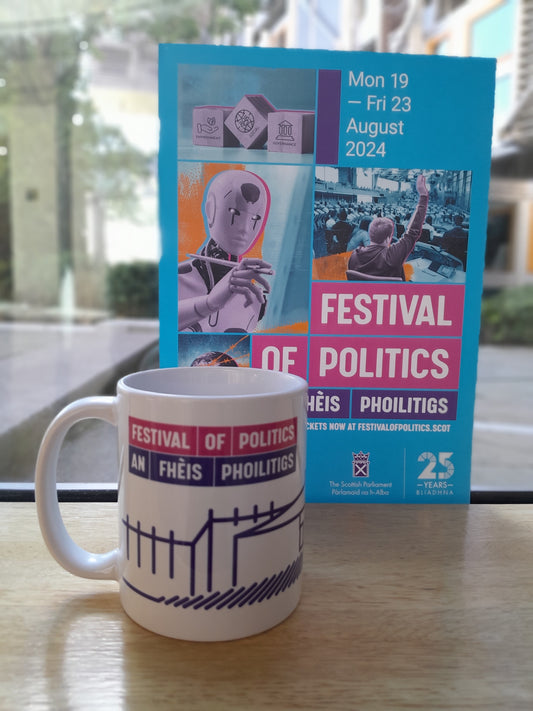 A white mug in front of a flier for the Festival of Politics 2024