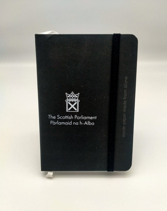 A black notebook decorated with the white symbol of the Scottish Parlaiment. Writing on the side says: inside paper made from stone.