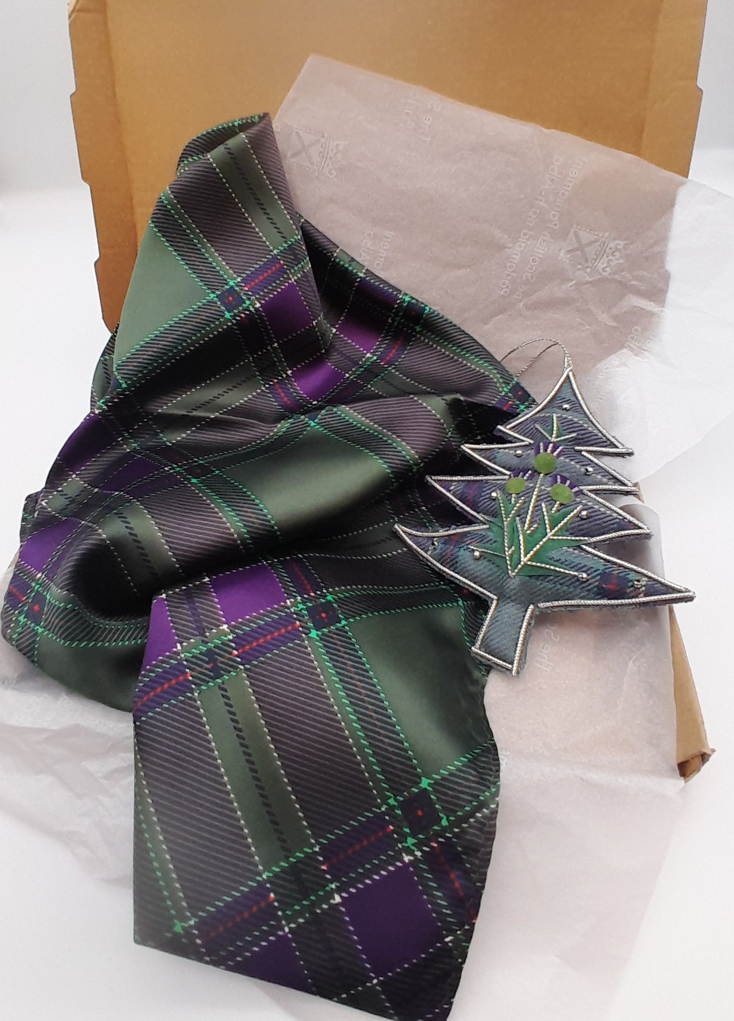 An open box with tartan scarf draped over it and a tartan Christmas tree decoration.