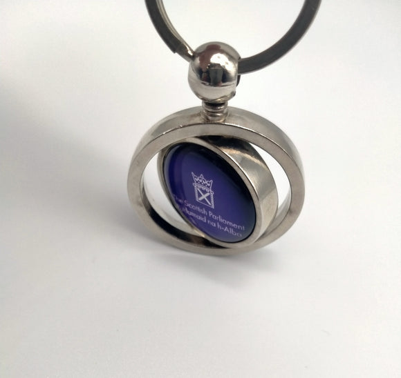 The keyring with the round spinning part showing the symbol of th Scottish Parliament on purple background.