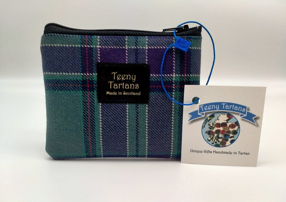 A rectangular purse made of the Scottish Parliament tartan with a black label in the middle. The writing on the lablel says: Teeny Tartans. Made in Scotland. A brand tag attached to the side.