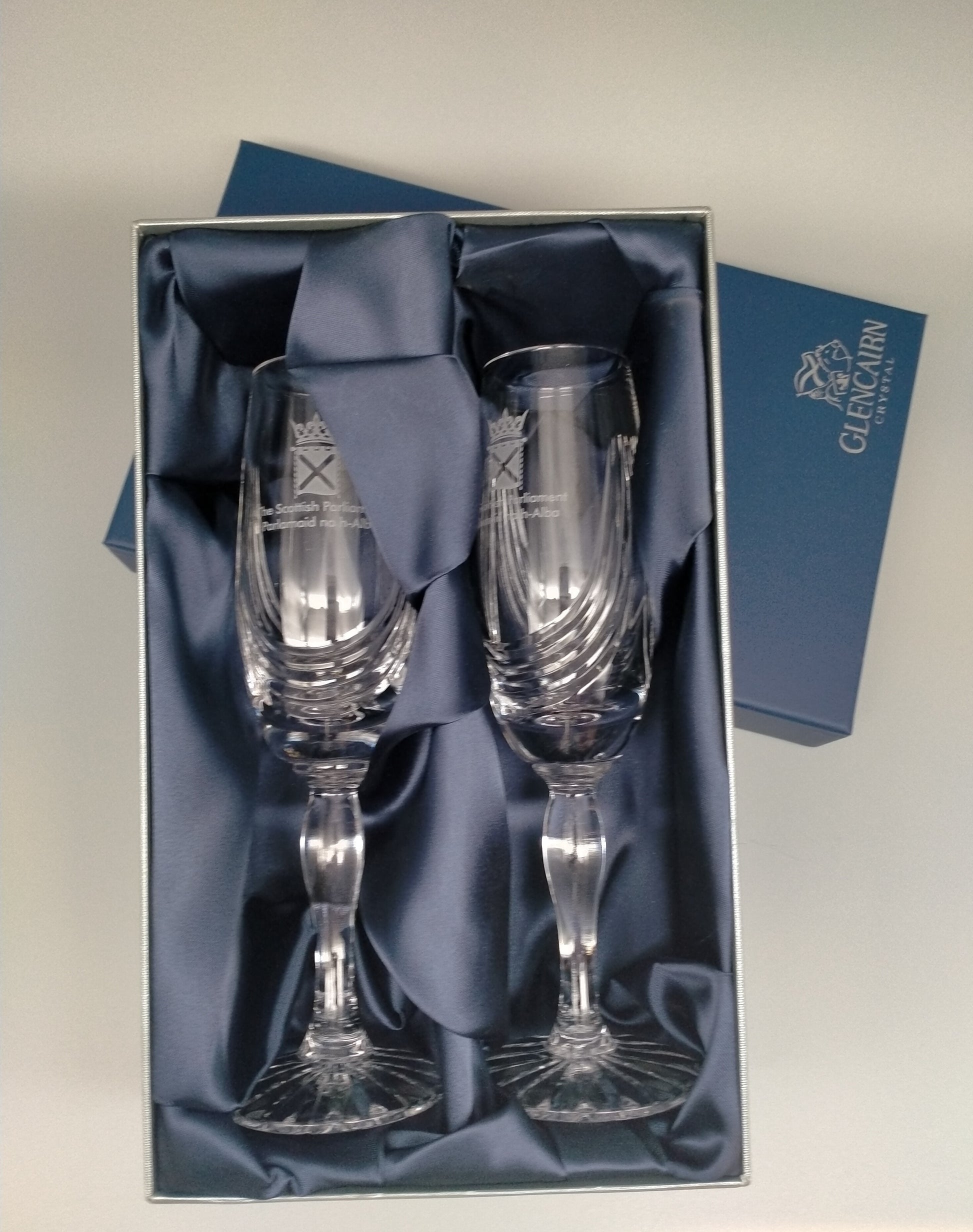 The pair of crystal flute glasses in a blue presentation box which is lined with navy blue fabric.