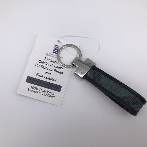 Chrome keyring with loop of tartan fabric edged with black leather. Tag attached reads Exclusive Official Scottish Parliament tartan and fine leather. Strip of printed tartan. 100% pure wool woven in Scotland.