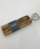 A bottle opener with a rectangular oak handle engraved with the Scottish Parliament building. In a black sleeve.