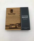 Square oak coasters engraved with the Scottish Parliament building and the parliament's logo. In the black sleeve.