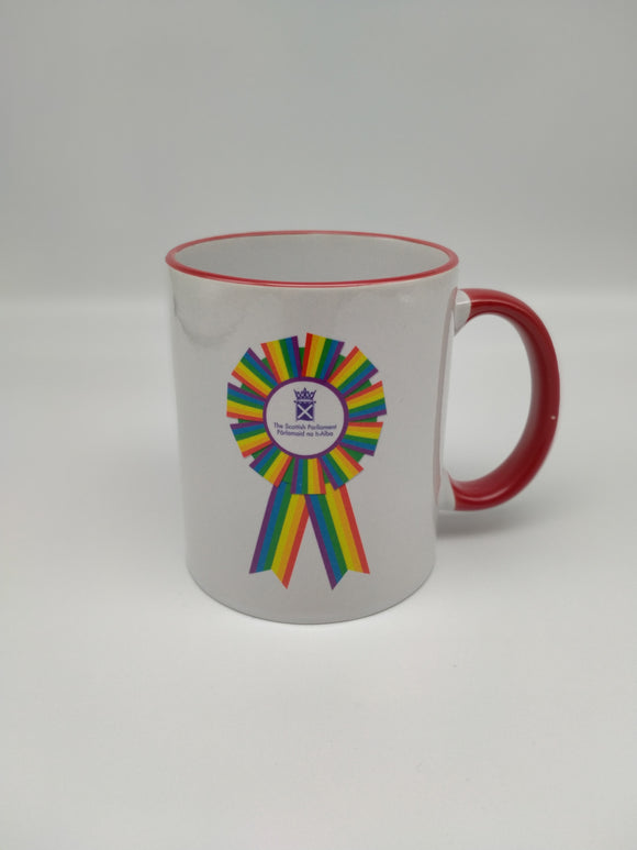 A white mug with a red handle, printed with a rainbow rosette with the purple symbol of the Scottish Parliament in the middle.