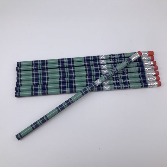 7 tartan pencils lying flat with another lying on top of them at an angle.