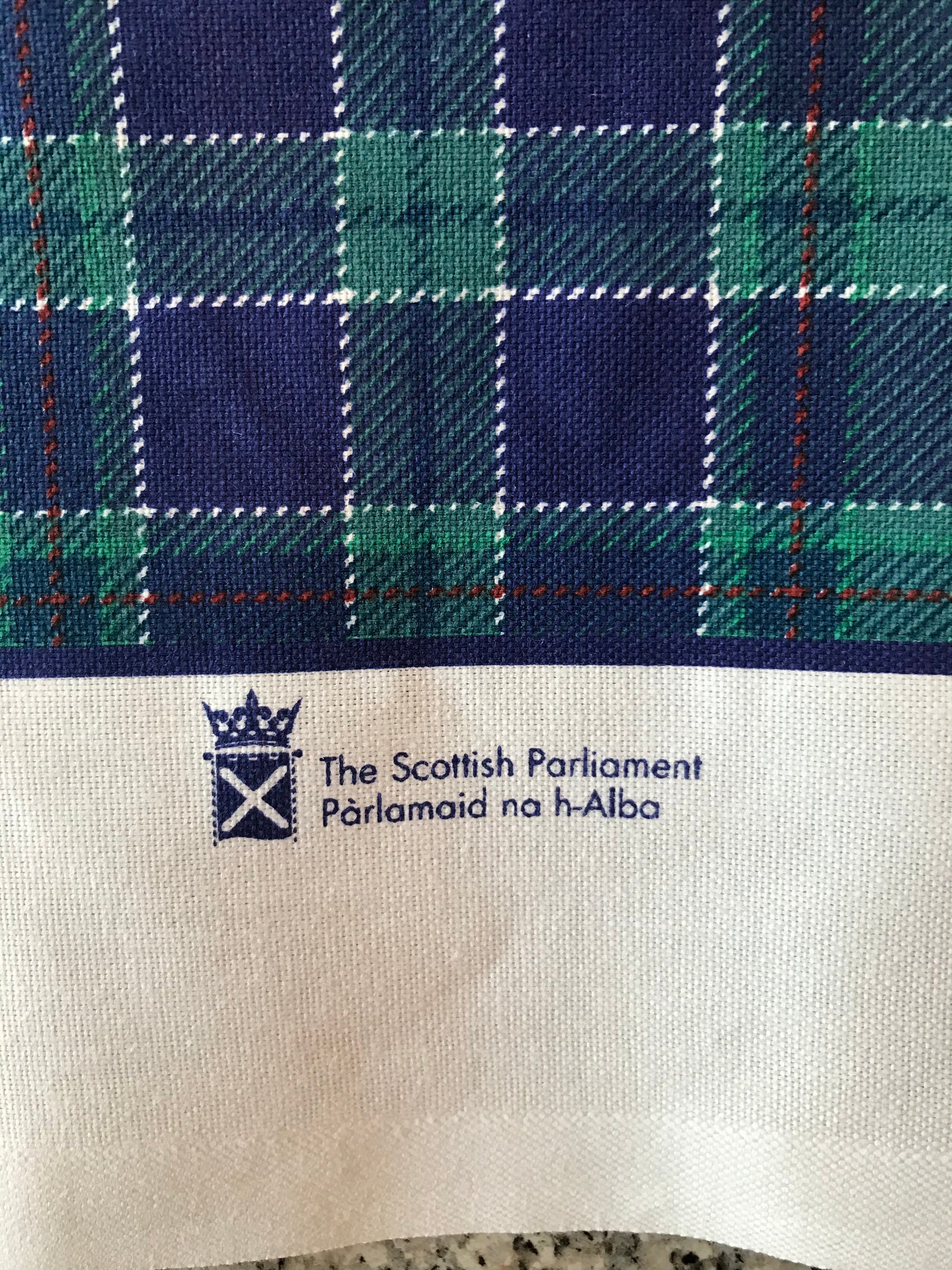 Close up of tartan tea towel showing symbol of Parliament printed on edge.