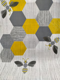 A section of printed tea towel showing bees and honeycomb design.  Grey, black and gold tones.