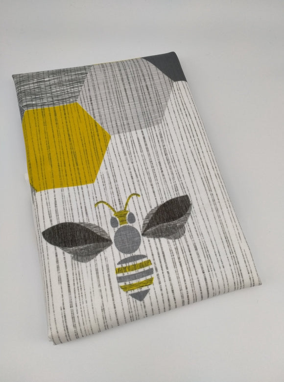 The tea towel folded showing a bee and hexagon shapes.  Grey, black and gold tones.