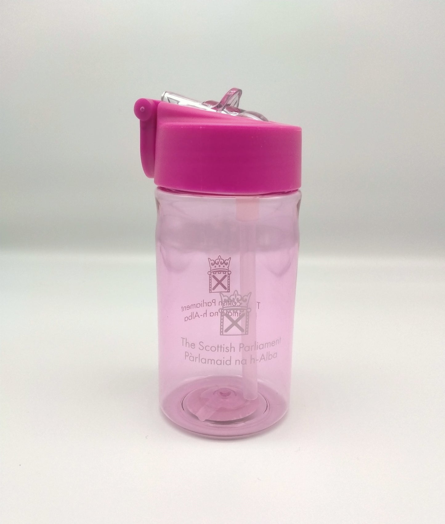 Transparent bottle tinted pink and decorated with the symbol of the Scottish Parliament. Lid is pink with a transparent pop-up spout.