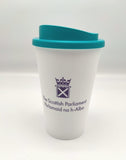 A white cup with a blue lid, decorated with the symbol of the Scottish Parliament in purple.