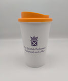 A white cup with an orange lid, decorated with the symbol of the Scottish Parliament in purple.