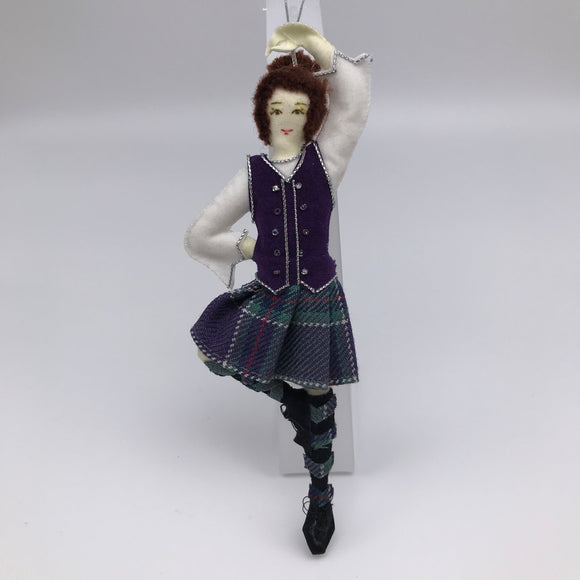 Highland dancer in dancing pose on one leg. Wearing Highland dress with tartan kilt and purple waistcoat.