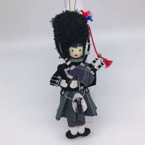Piper in full Highland dress with tartan kilt and bagpipes. Wearing a black "bearskin" style hat. Silver and red thread decoration.