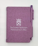 A purple notebook with the symbol of the Scottish Parlaiment in white and a matching pen slid into a holder on the side.