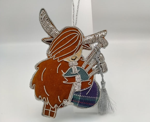 Brown highland cow playing tartan bagpipes. Decorated with silver stitching and a silver tassel. 