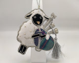 A sheep playing tartan bagpipes. Decorated with silver stitching and a silver tassel.