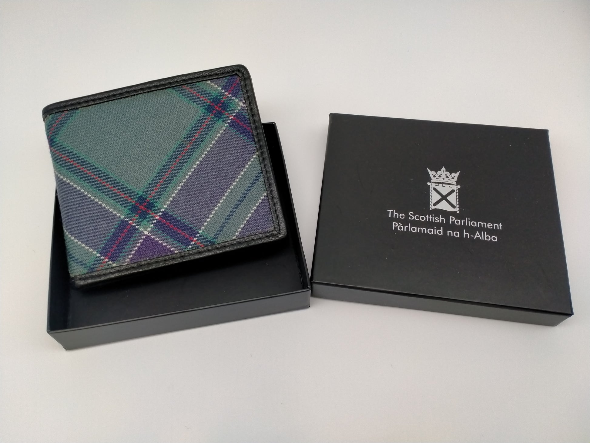 The wallet in its black box. Lid decorated with the symbol of the Scottish Parliament. printed in silver.